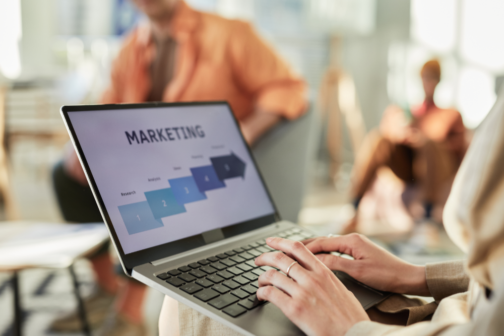A woman sits on a chair in the foreground and write on a laptop about financial advisor digital marketing
