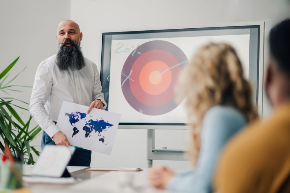 A bearded man points to a whiteboard, explaining the financial advisor sales funnel to his colleagues
